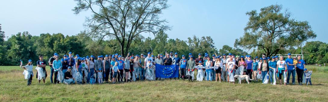 A group of over 100 people stand in a field holding up an EU flag.