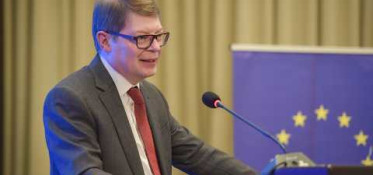 White man in glasses is speacking in front of a microphone