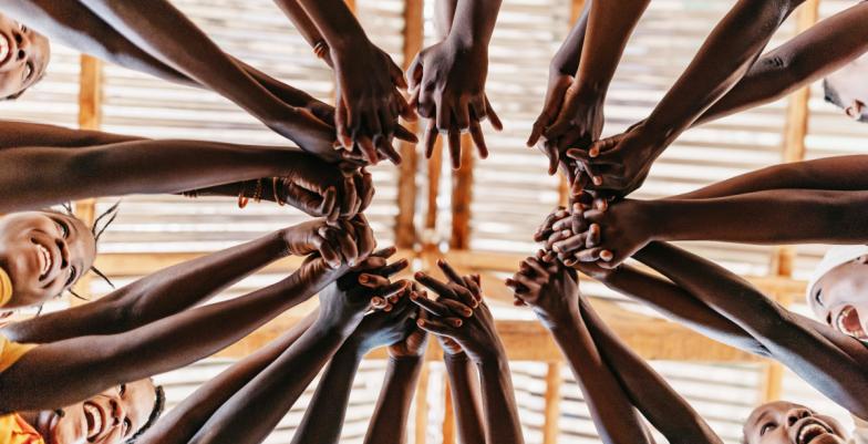 Low angle of children standing in a circle reaching out to join hands.
