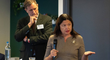A speaker in foreground with the chairperson in background listening closely.