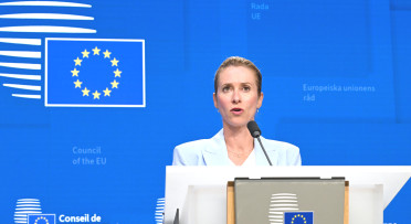 Kaja Kallas stands against a blue EU background. 