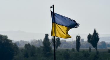 Tattered Ukraininan flag flies above a battlefield on a grey day.