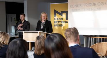 woman speaking at a podium in front of guests. A sign language interpretor to the left. 