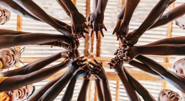 Low angle of children standing in a circle reaching out to join hands.