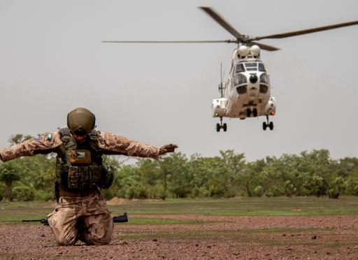 a soldier on his knees on the ground and a helicopter behind him
