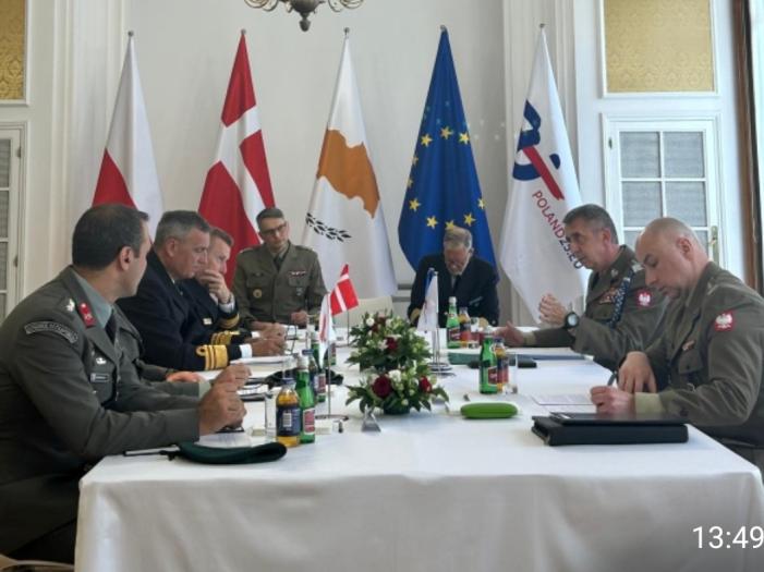 People in uniform having a meeting with some flags behind.