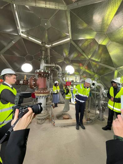 People in bright yellow jackets standing inside a small, aluminium covered carbon capture facility