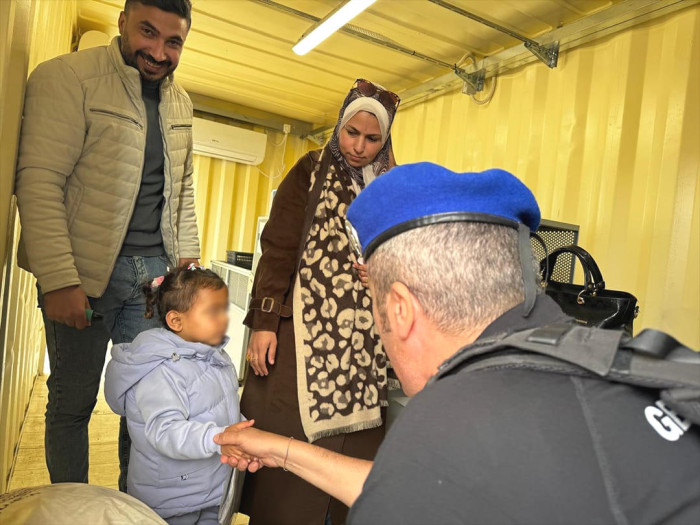 Interior, parents and their young child are greeted at the border crossing. 