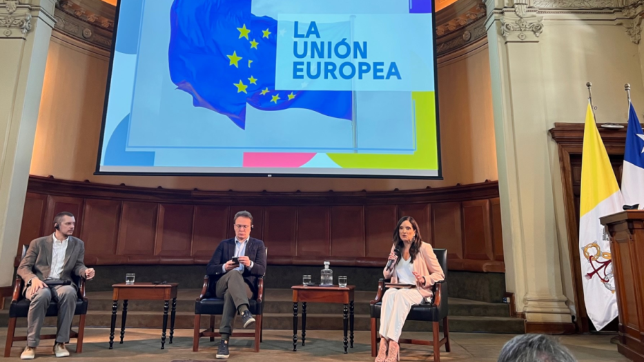 Three people on stage beneath projection of EU flag