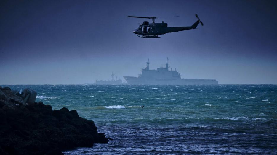 Foreground, an air unit approaches the coastline, background two naval combat ships stand off for amphibious assault.