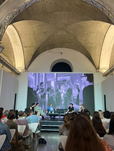 Interior of a conference hall with a panel on stage addressing the audience. 