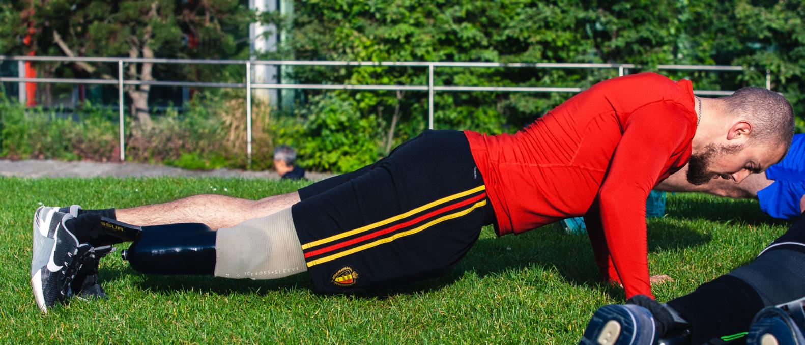 Athlete in red jersey warms up with push-ups, prosthetic leg visible. 