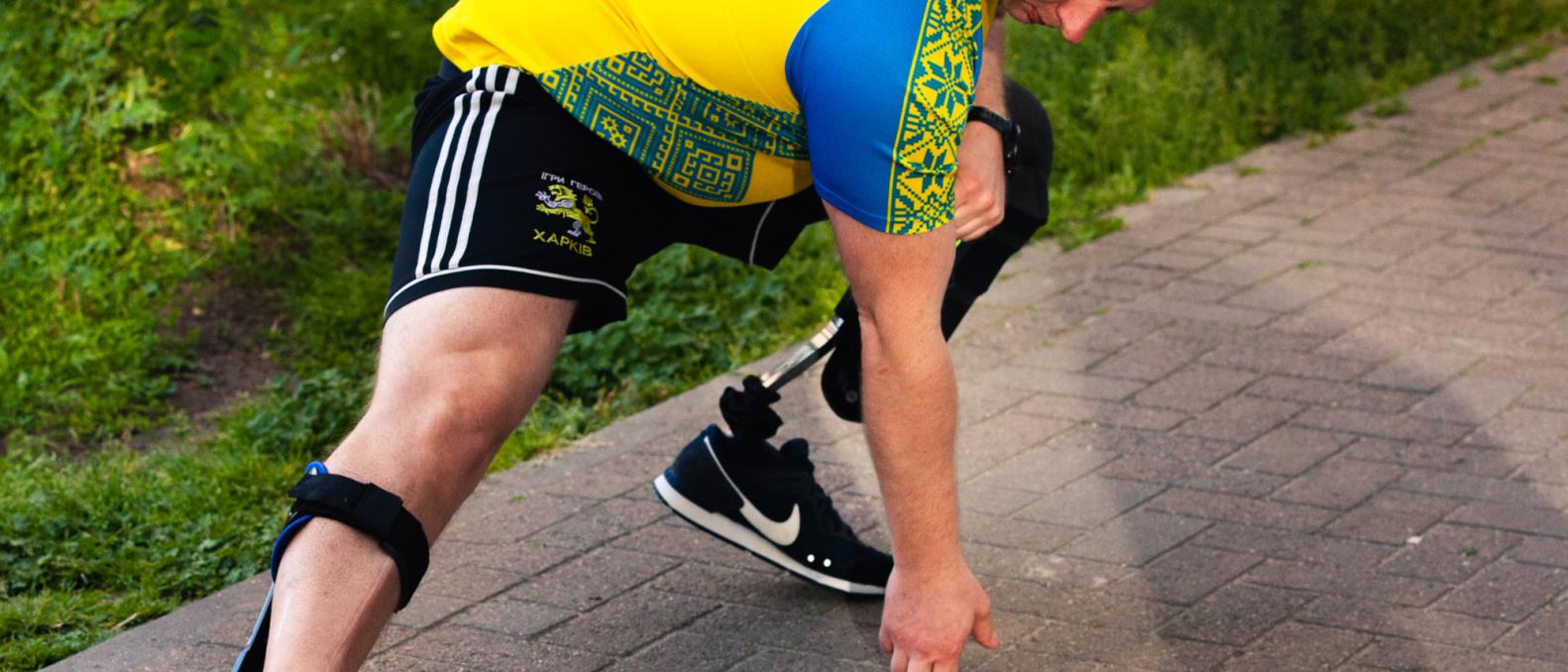 Athlete in yellow jersey stretches before run, prosthetic leg visible.