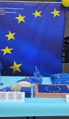 Photo of the EU booth at an event. Large EU banner in the background, with flags and decorated cakes