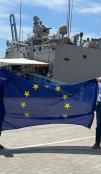 People hold EU flag with naval ship in background