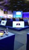 A VIP addresses a forum while appearing on several screens.