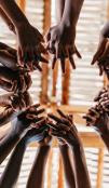 Low angle of children standing in a circle reaching out to join hands.