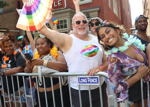 A man in a white tank top holding a rainbow fan.