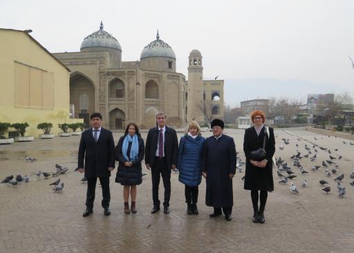 A group of six people posing for the camera in front of a mosque. A lot of pigeon in the ground.