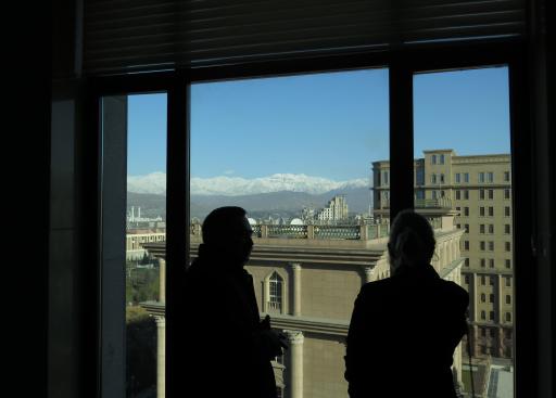 Silhouettes of two people looking out the window towards tall buildings and mountains in the back.