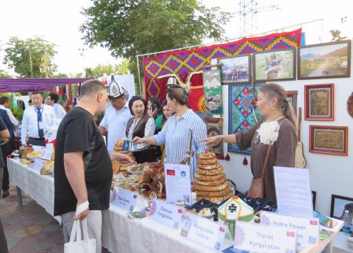 Several people behind a stand filled with different breads and nametags. Behind them hang pictures and fabrics. One person on the other side of the stand pointing to one bread.