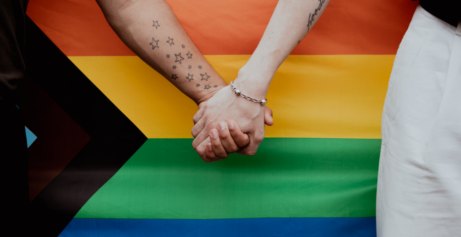 People holding hands in front of a Rainbow Flag