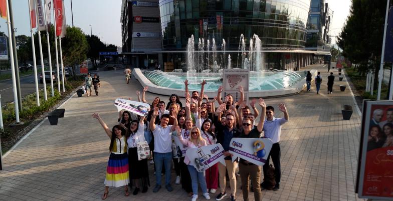 Group of people cheering and standing on a square in front of a fountain
