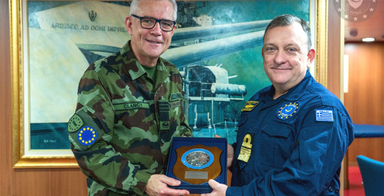 Two military men smile at the camera indoors while awarding a medal. 