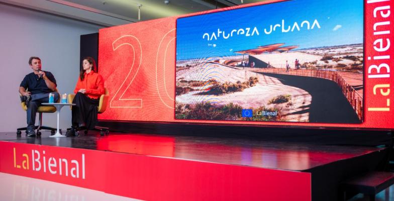 Stage at a conference with two people seated, sign says "Bienial".