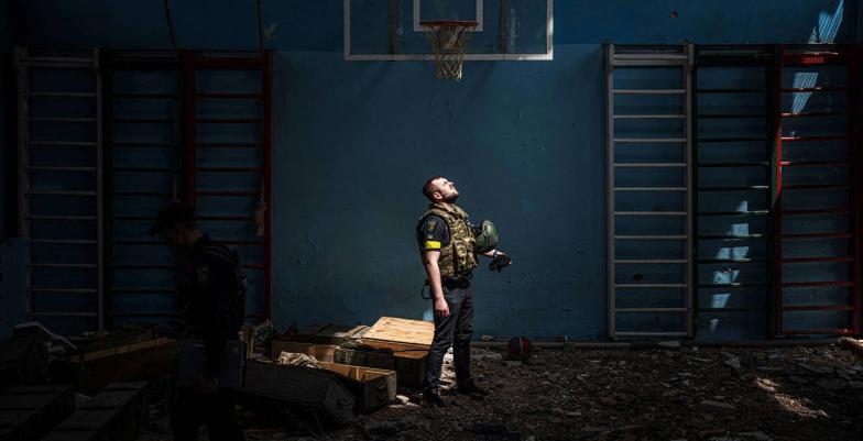 A lone Ukrainian soldier standing in a dark room looks up at a skylight.