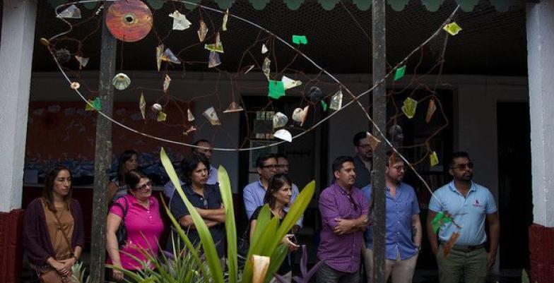 Group of people standing under the roof of a patio with a sculpture.