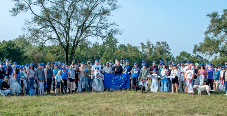 A group of over 100 people stand in a field holding up an EU flag.