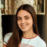 Young girl with long brown hair posing in front of the camera with a smile.