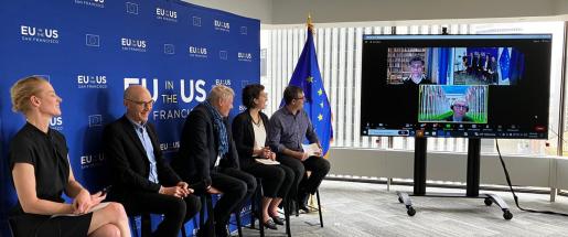 Four people sit on stools during a panel with three people presenting on screen to the right.