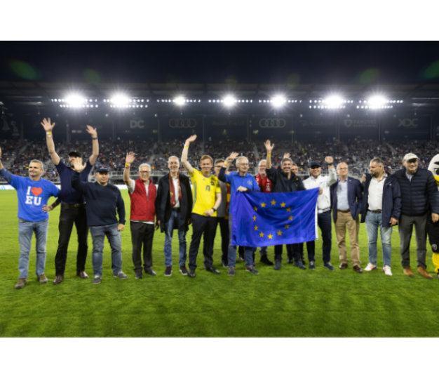 Several EU Ambassadors wave on the field of a soccer match.