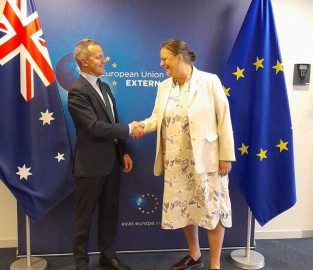 A man and a woman shake hands as they meet indoors in an office.