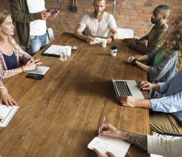 A diverse group of six people in a meeting around a desk. 