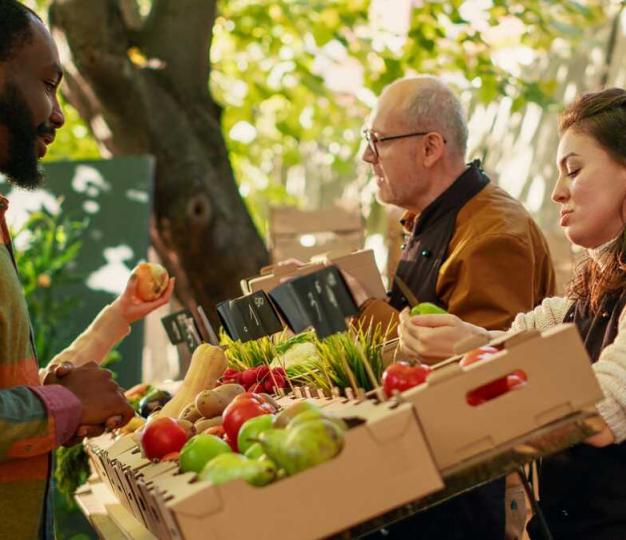 A vegetable seller talking with a customer at an open air market.