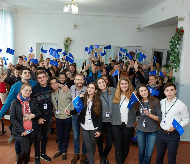 Indoors, large group of young people waving EU flags enthusiastically.