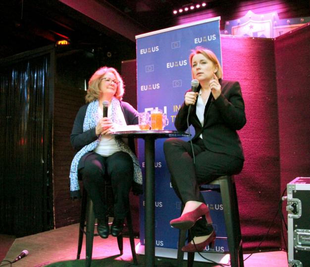 Two women seated at a bar top table on a stage.