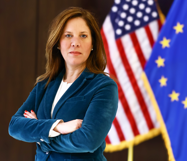 Woman in blue blazer poses in front of US and EU flags
