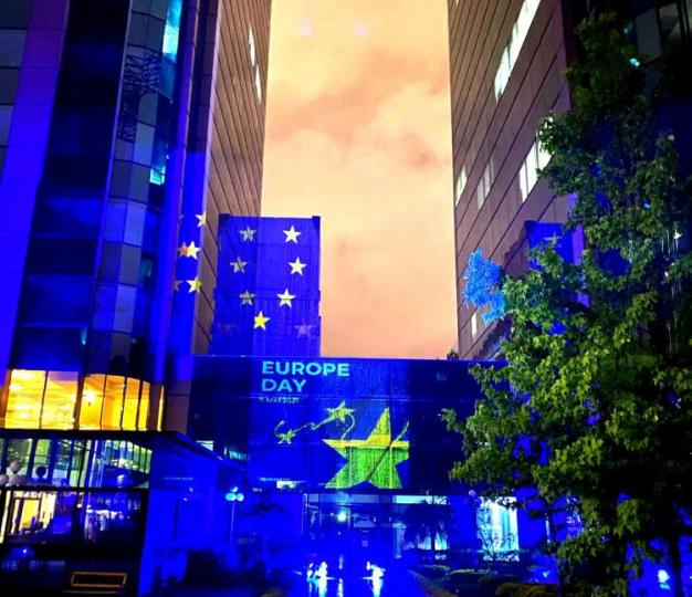 Night picture of building illuminated with blue lights and yellow stars on the occasion of Europe Day. Yellow stars and the words Europe Day are projected on the glass windows of the building.  